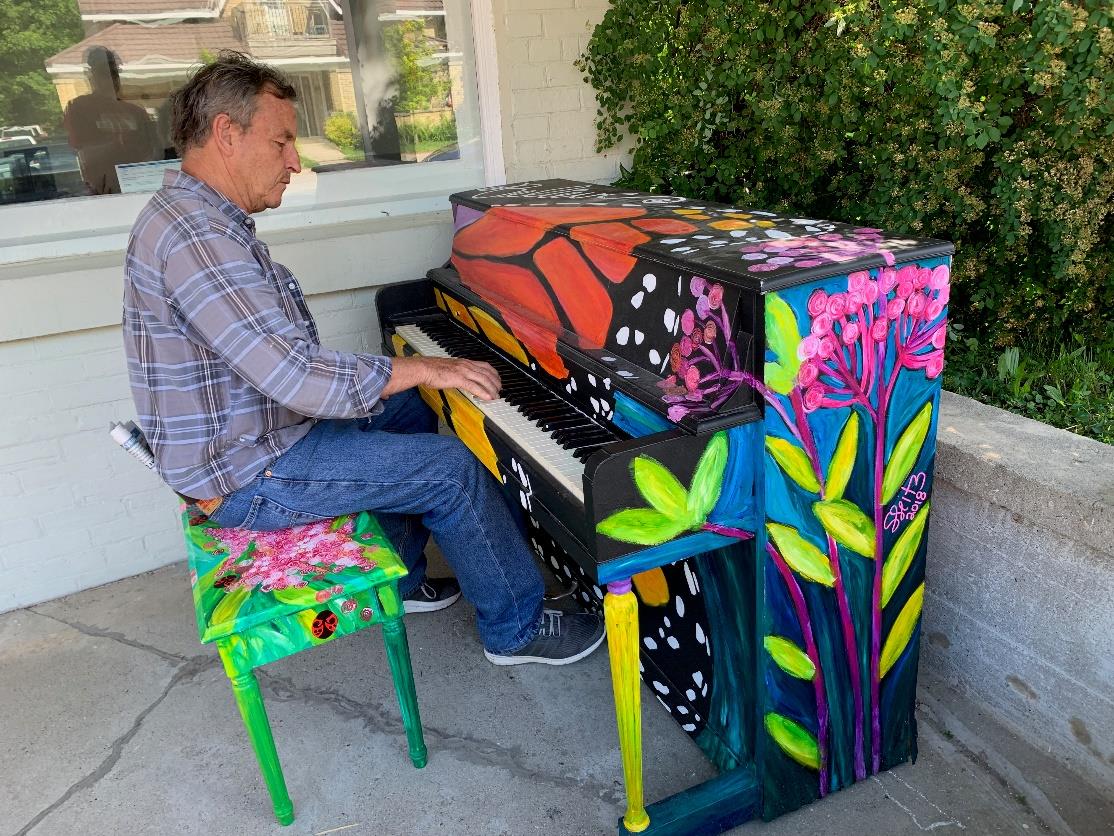 man playing colourful painted piano on a patio