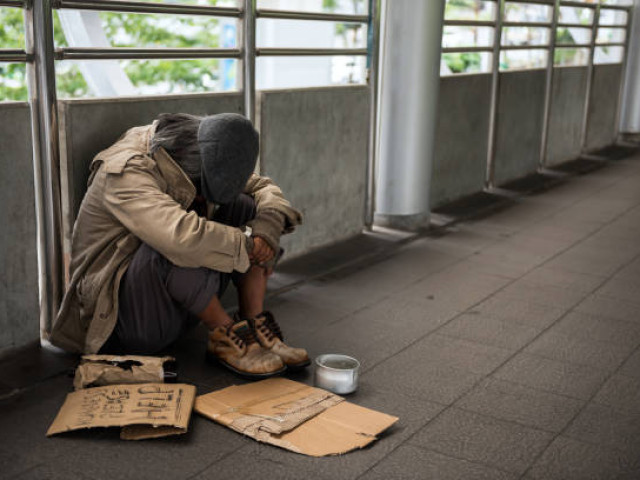 a person experiencing homelessness crouched against wall with cardboard help signs and tin can