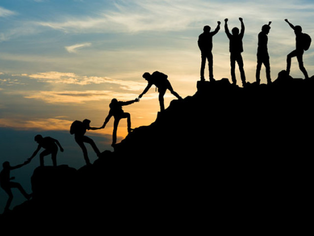 hikers helping each other to climb a mountain