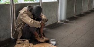 a person experiencing homelessness on a walkway with a can and a sign