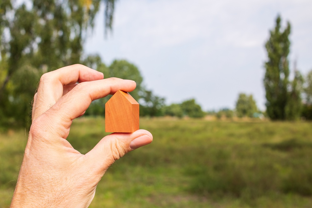 hand holding tiny wooden house in front of a field
