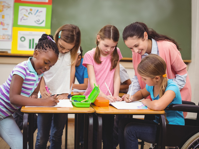 Teacher and young students around a desk.