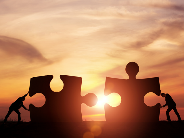 two people pushing giant puzzle pieces together in front of a sunset