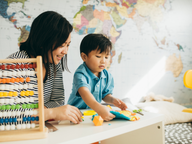 woman sitting with child playing with toys at table with map of the world in the background