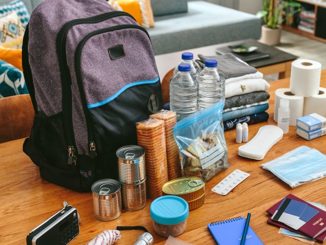 Backpack with emergency supplies laid out on table including water, canned food, matches and more