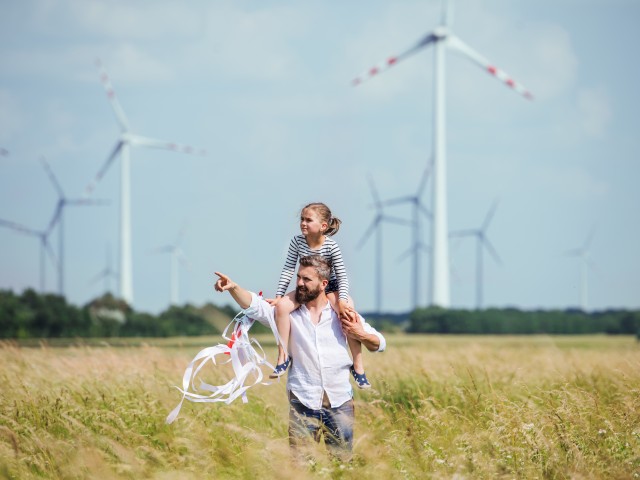 Man and girl walking through field, man pointing, wind turbines in background