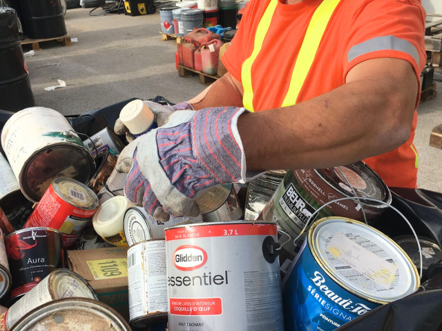 A person with work gloves sorting through pile of old paint cans