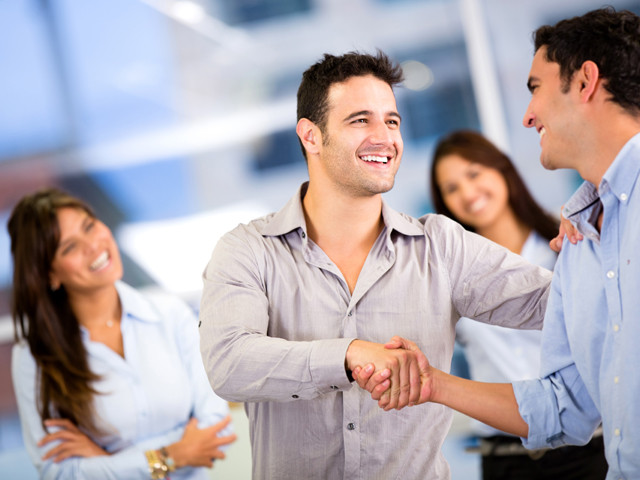 two people shaking hands with other people smiling around them