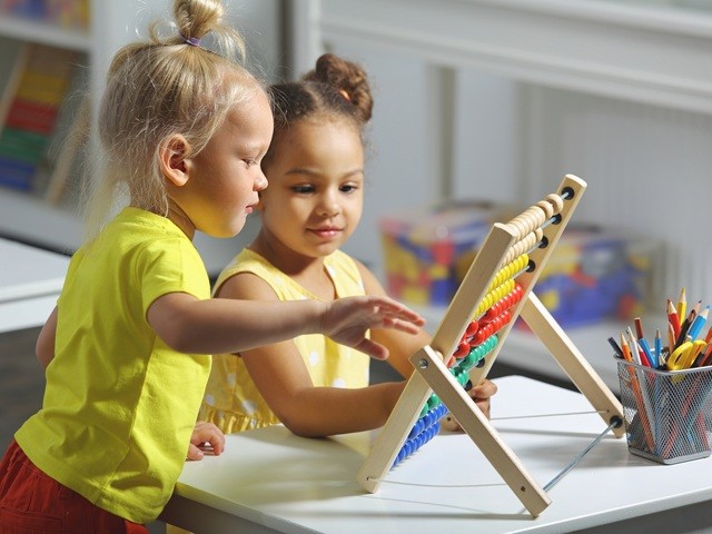 Two children sit together at the table and count on the abacus and smiles.