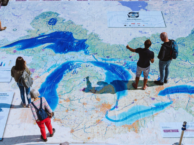 People standing on a floor map focused on the Great Lakes.