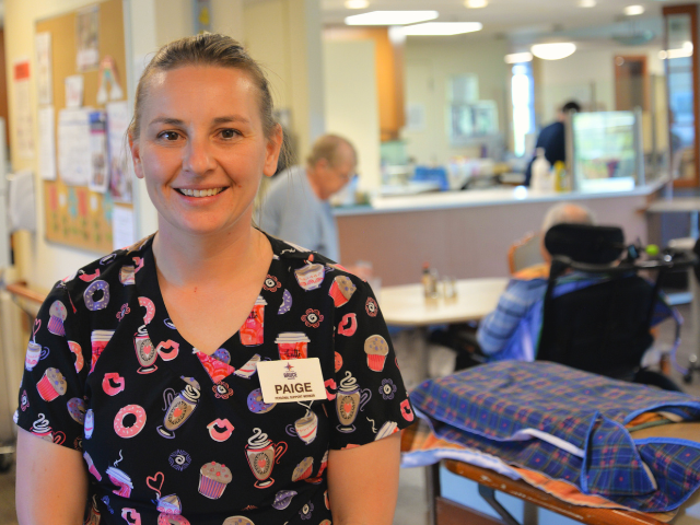 Woman PSW in front of lunch room with residents in background at Brucelea Haven