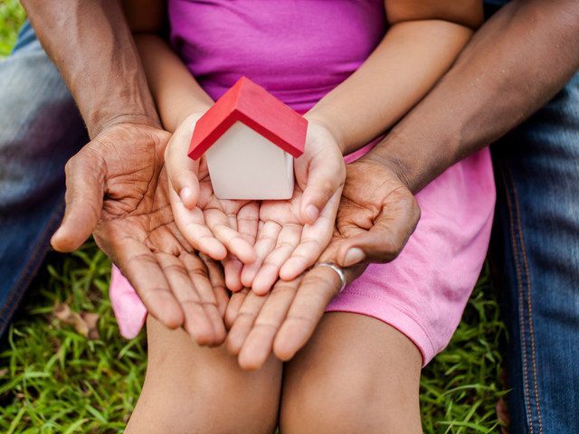 a child holding a tiny birdhouse while an adult holds around the child's hands