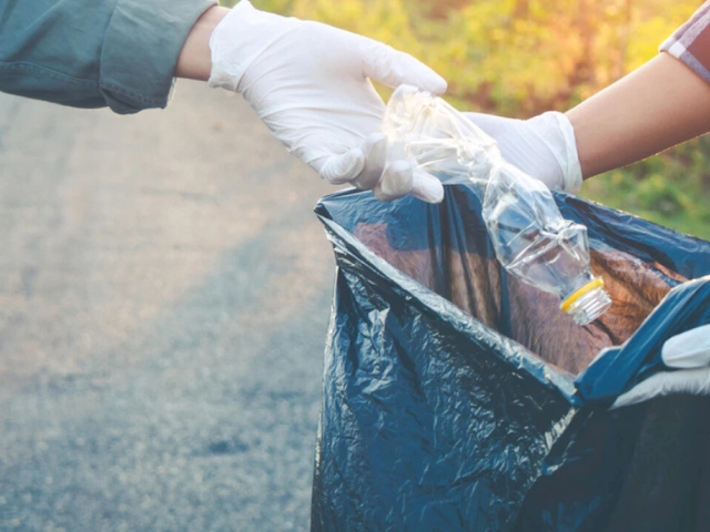 Hands with white gloves on picking up trash and putting into trash bag