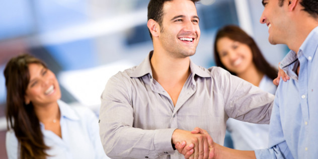 two people shaking hands with other people smiling around them